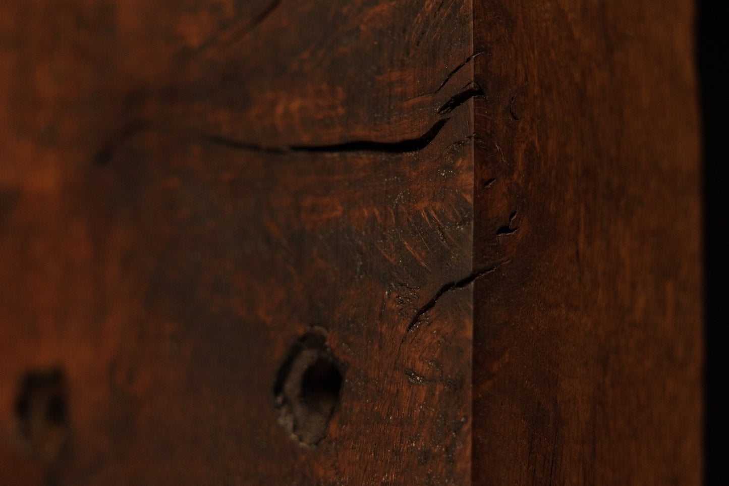 Macro view of the dark architectural salvage wood edge highlighting deep soil mineral absorption and authentic organic patina. 