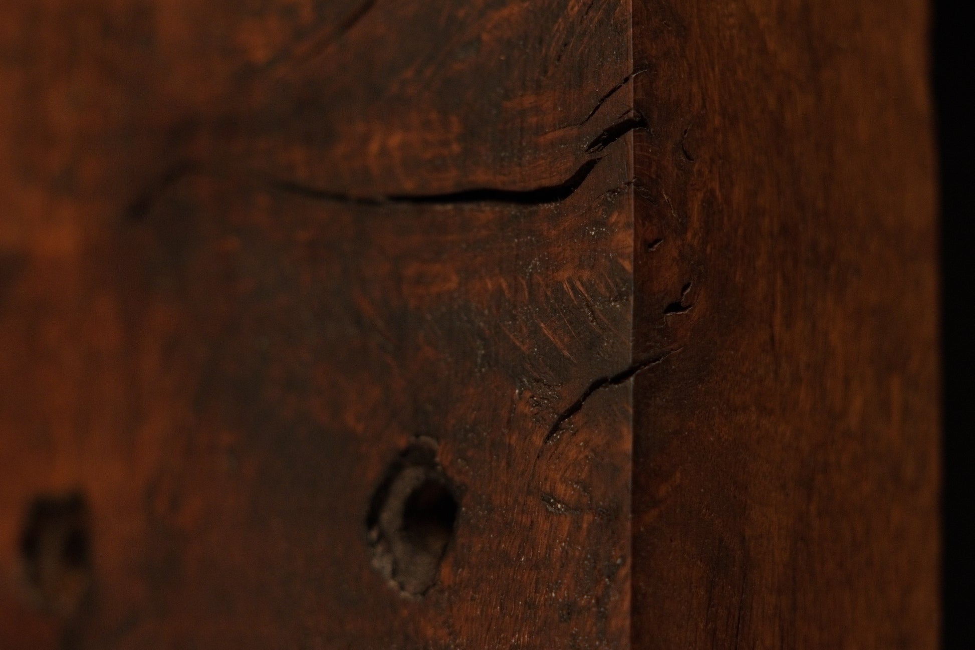 Macro view of the dark architectural salvage wood edge highlighting deep soil mineral absorption and authentic organic patina. 