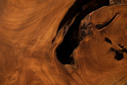 Close-up of a dramatic dark organic void opening up between smooth flowing golden-brown wood grain sections on the medium sculpture.