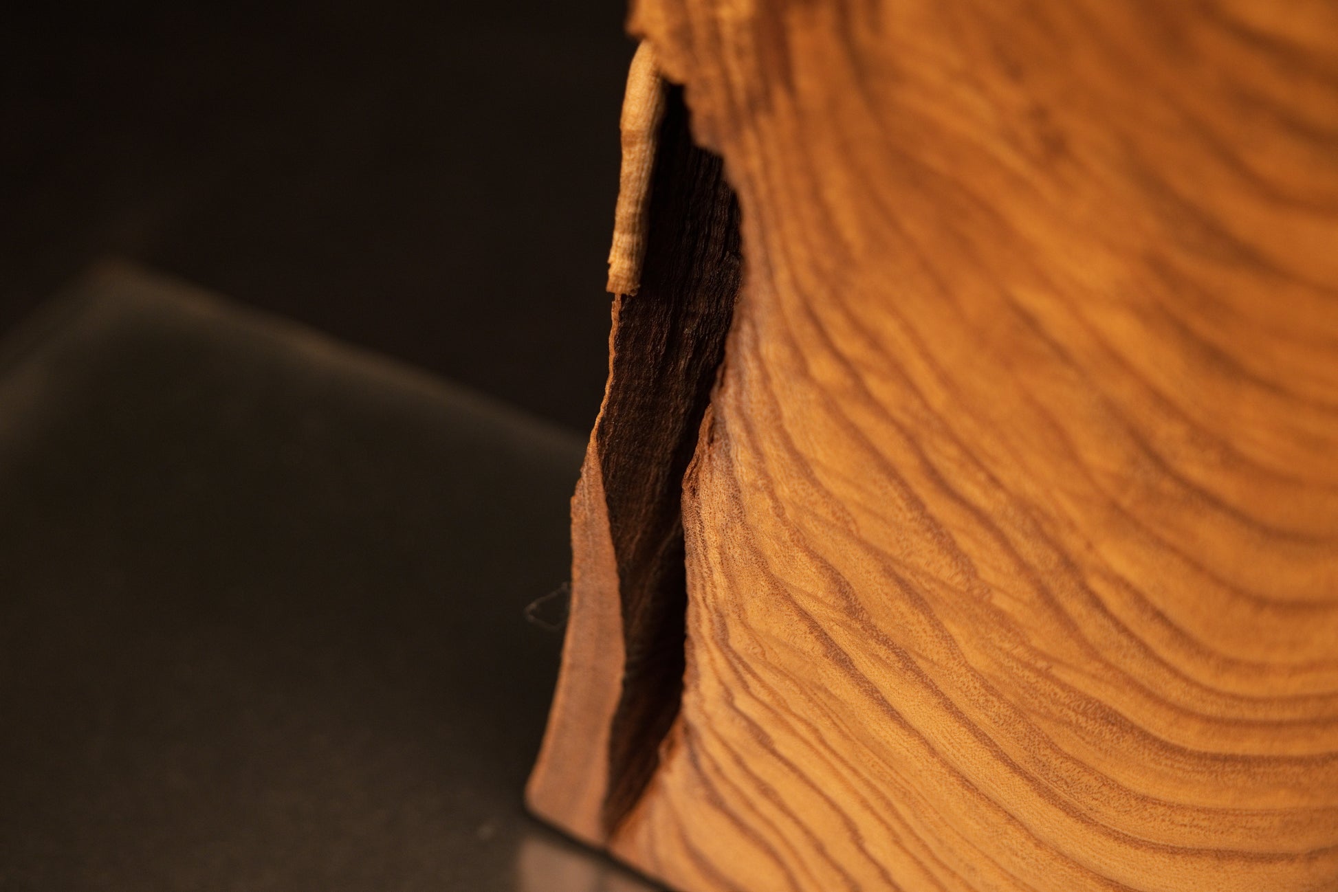 Close-up perspective of a narrow vertical opening and deep dark shadow recess running along the side of the medium oak sculpture.