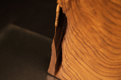 Close-up perspective of a narrow vertical opening and deep dark shadow recess running along the side of the medium oak sculpture.