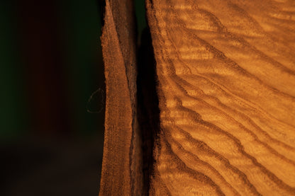 Macro view of a narrow dark gap between two massive vertical wooden blocks showing rich chatoyant grain patterns on the sculpture.