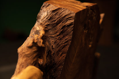 Macro view of a heavy solid wooden block highlighting deep organic textures, dark knots, and warm golden-brown wood coloration.
