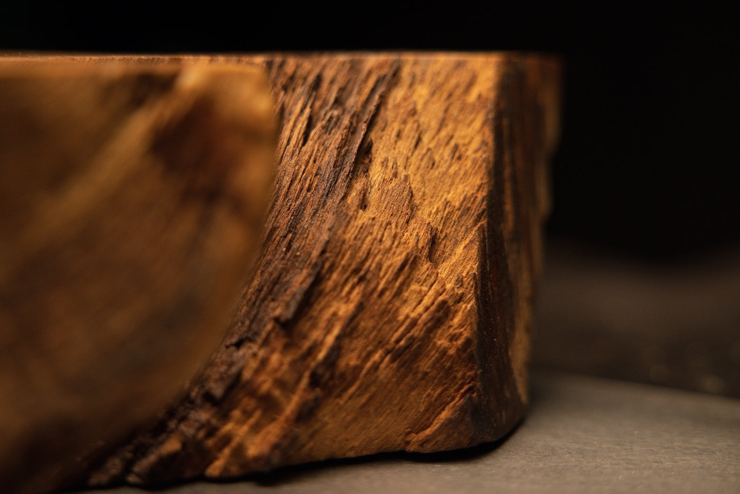 Macro view of rugged rough timber texturing and deep weathered grain lines along the bottom corner edge of the medium oak sculpture.