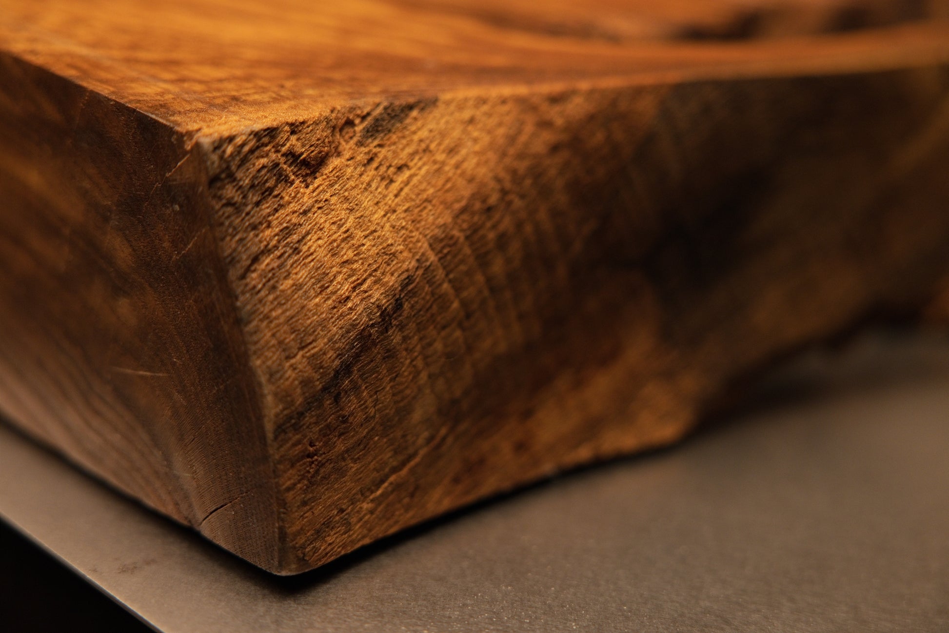 Angled macro shot of a solid wooden block corner showing precision cut angles and rich golden-brown grain textures on the artifact.