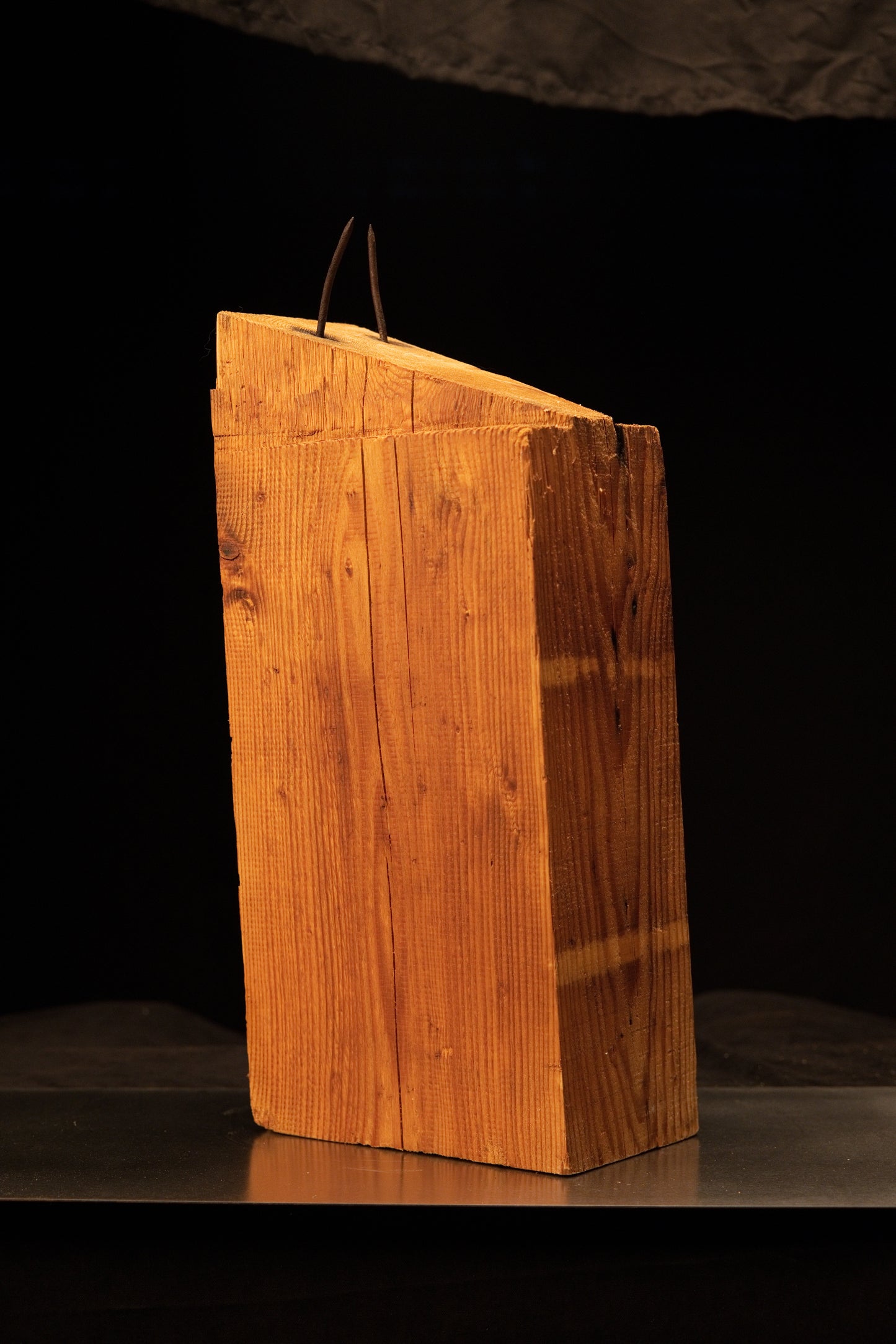 Angled front view of a century-old structural timber beam displaying vertical wood grain and original architectural metal spikes.   