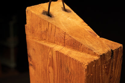 Macro detail of the slanted top on a heritage structural monolith showcasing dense end-grain and embedded historic iron spikes.   