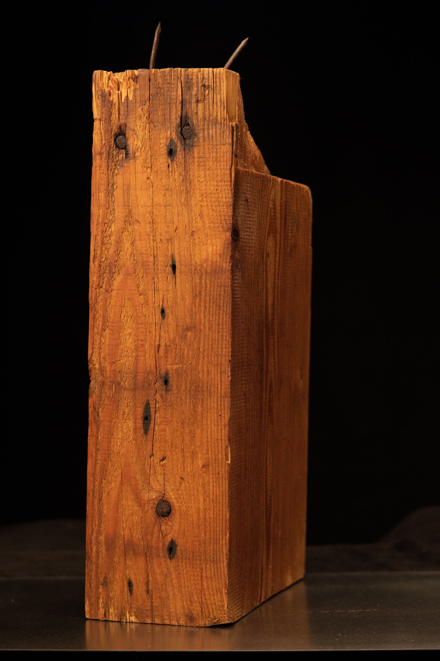 Standing profile view of a structural historic timber block featuring original embedded iron spikes and a crack-resistant body.   