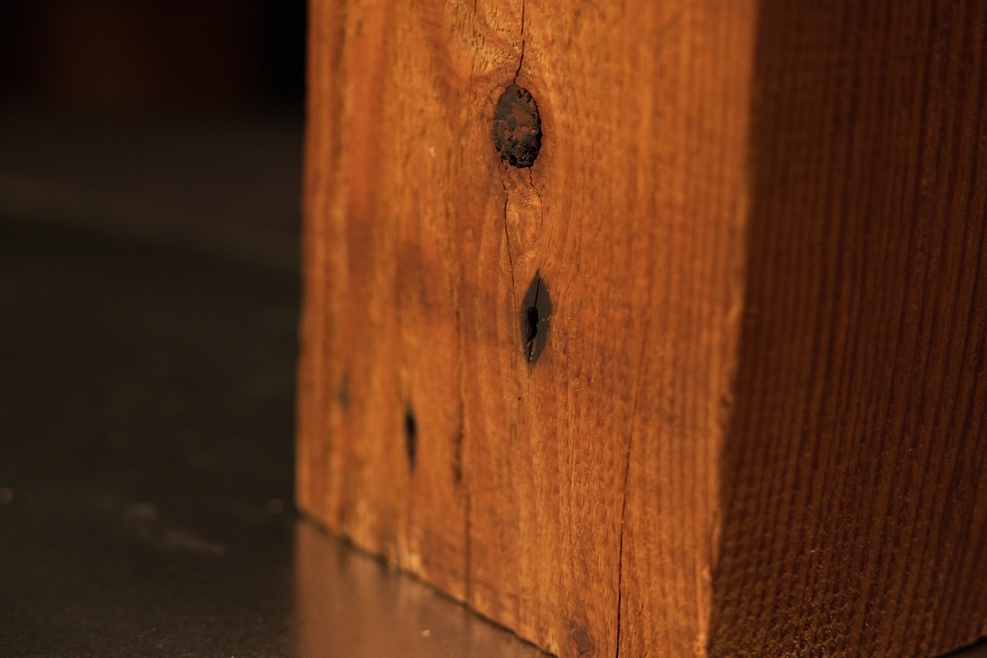Close view of authentic dark structural knots and joinery voids embedded in a fully stabilized architectural salvage timber beam.   