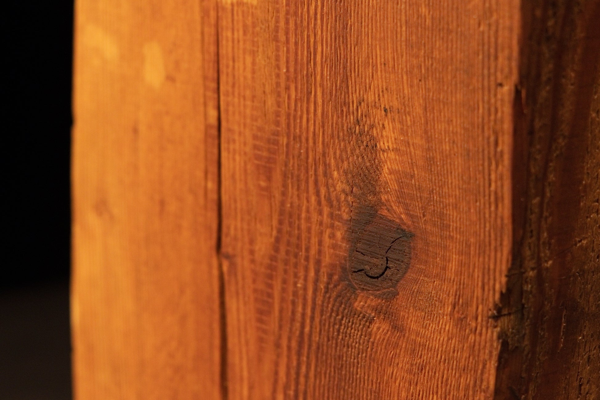 Extreme close-up of a dark organic knot within a golden architectural salvage timber piece demonstrating true structural mass.   