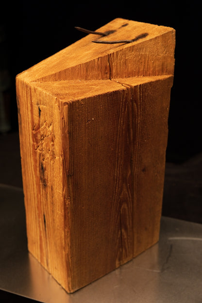 Detailed front view of a thick-cut monolithic timber block revealing a slanted upper cut and two century-old rusted iron nails.   