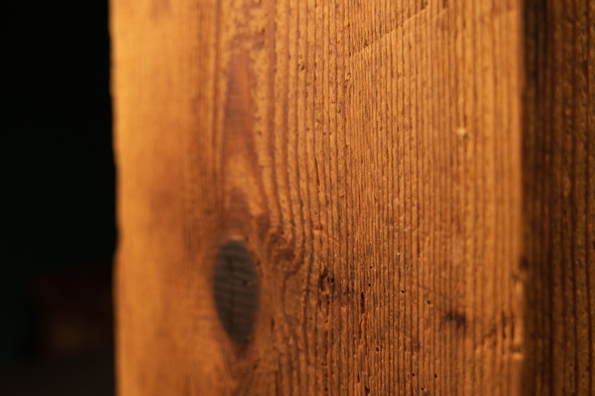 Macro detail of a large prominent dark knot near the base of an epoxy-free historic wood beam showing raw botanical textures.   