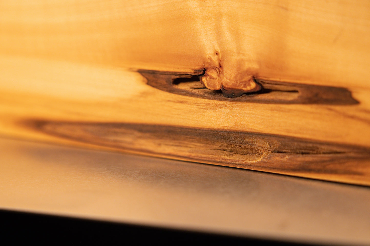 Front view of a tall, polished architectural wooden monolith displaying smooth golden grain and a dark wavy botanical edge.   