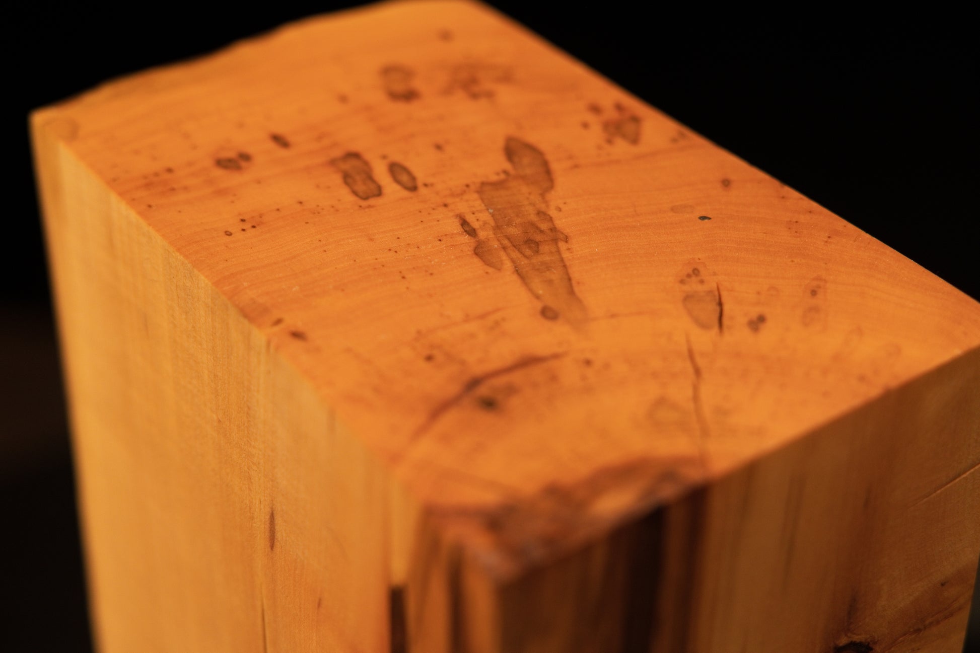 Macro focus on a small, dark organic knot seamlessly embedded within the vertical golden grain of the structural wood piece.   