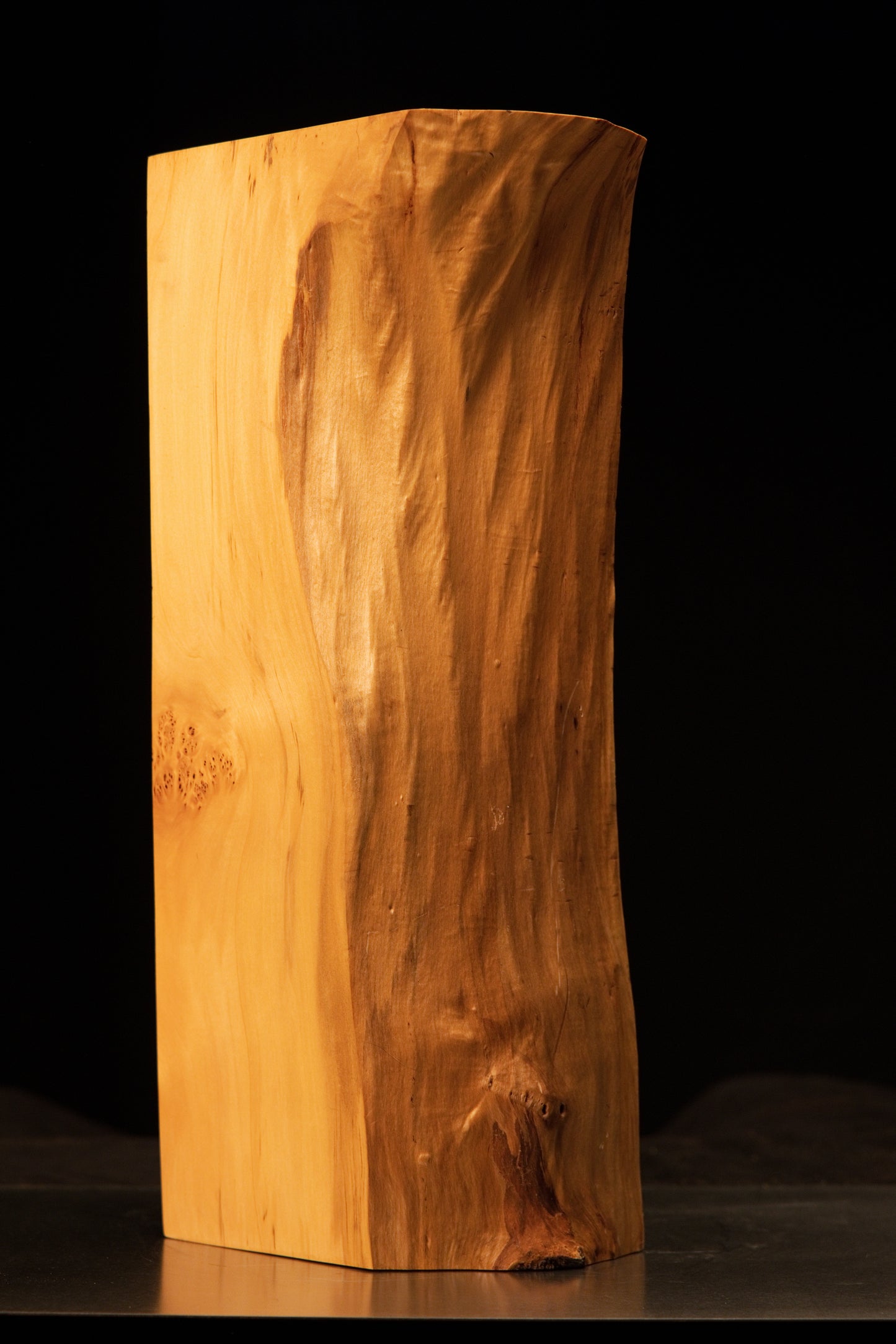Angled view of a polished architectural wooden monolith highlighting a heavily sculpted wavy face and true organic geometry.   