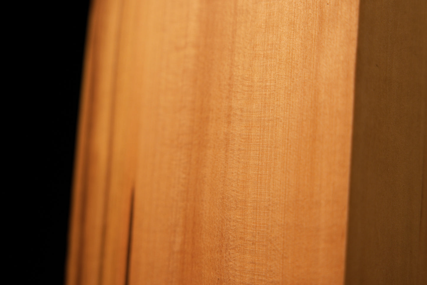 Macro photography of wavy golden grain and authentic chatoyancy on the polished surface of a heritage structural wood slab.   
