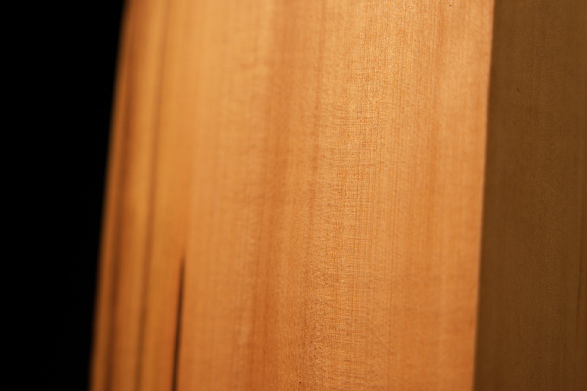 Macro photography of wavy golden grain and authentic chatoyancy on the polished surface of a heritage structural wood slab.   