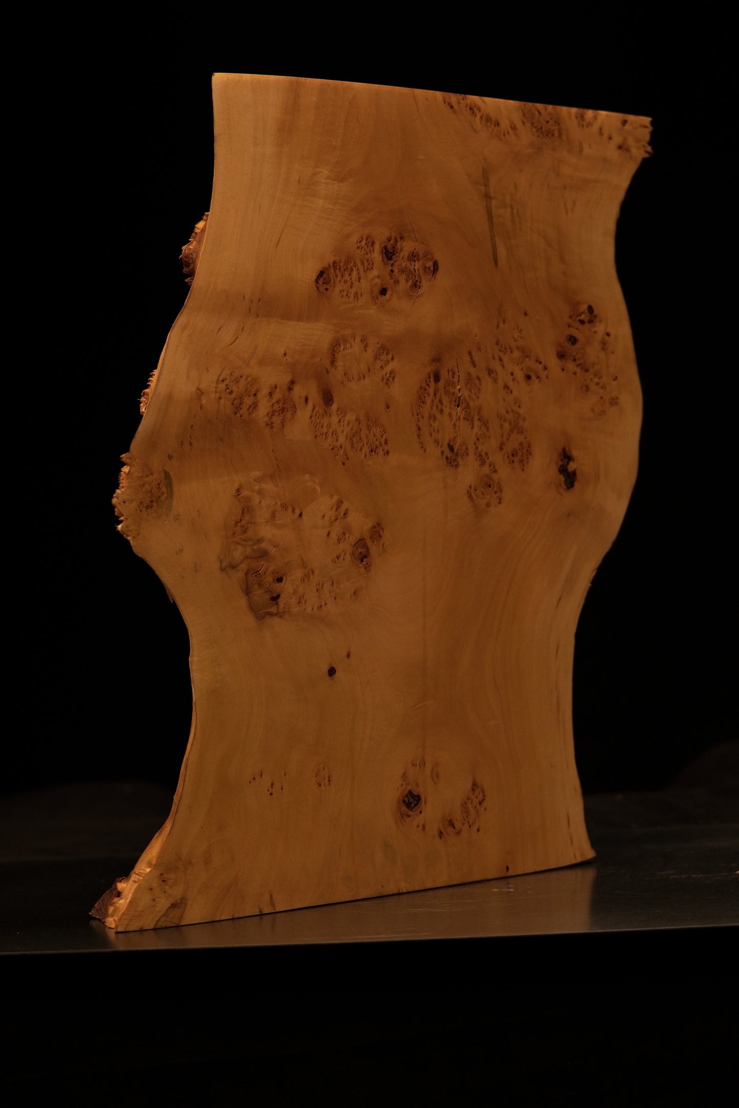 Detailed macro side perspective view highlighting a prominent dark wood knot near the polished bottom edge of the sculpture.   