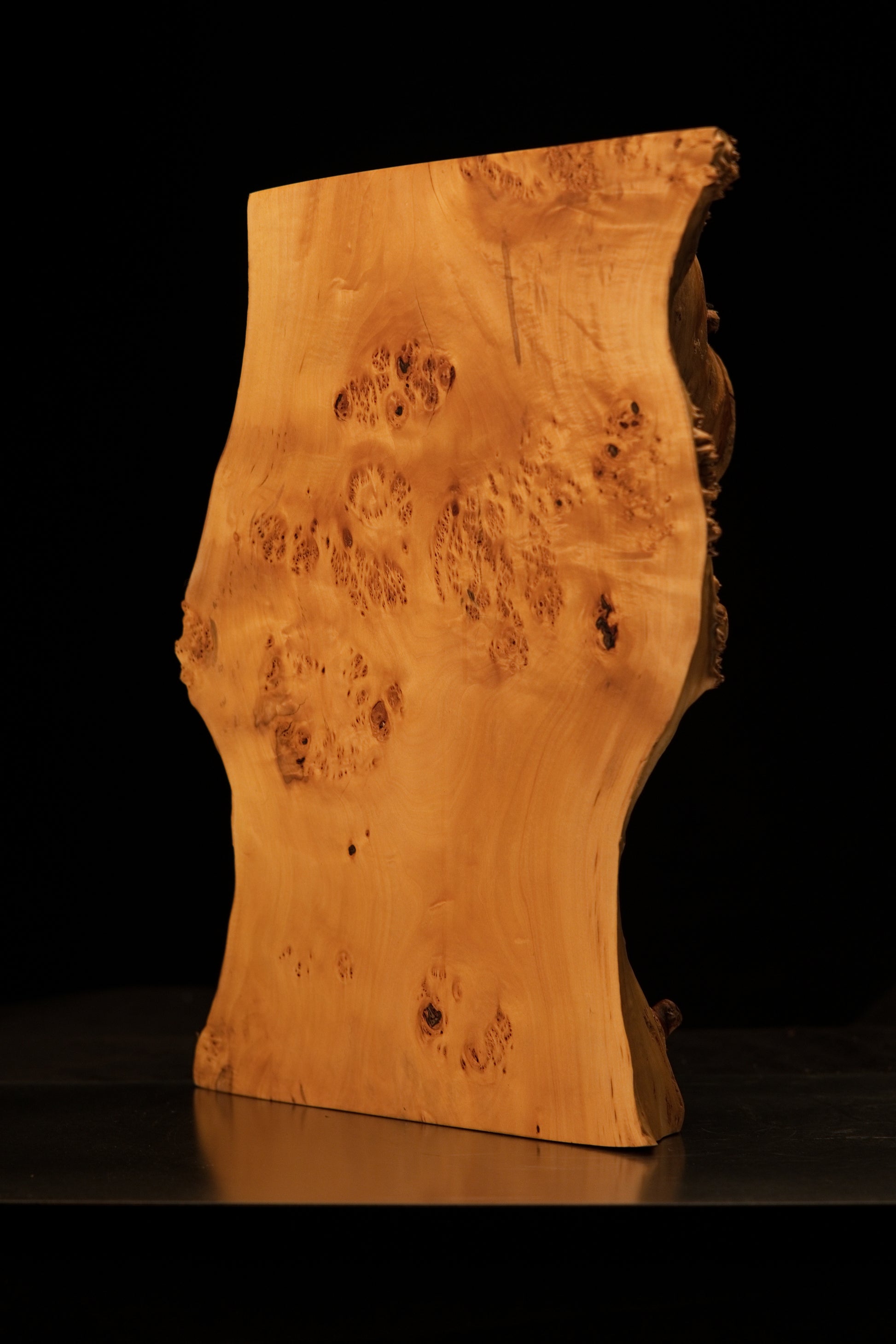 Detailed close-up macro photograph of the bottom right corner edge showing smooth wood flowing downward onto the metal base.   