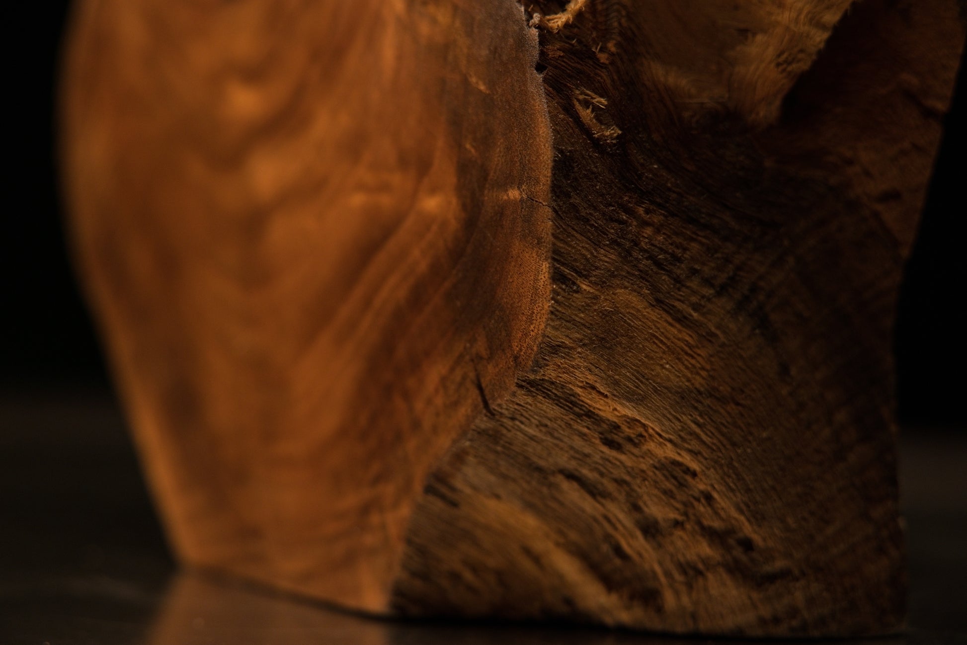 Broad lateral profile of a carved wooden display featuring a level base cut and deep organic shadow cavities above.   