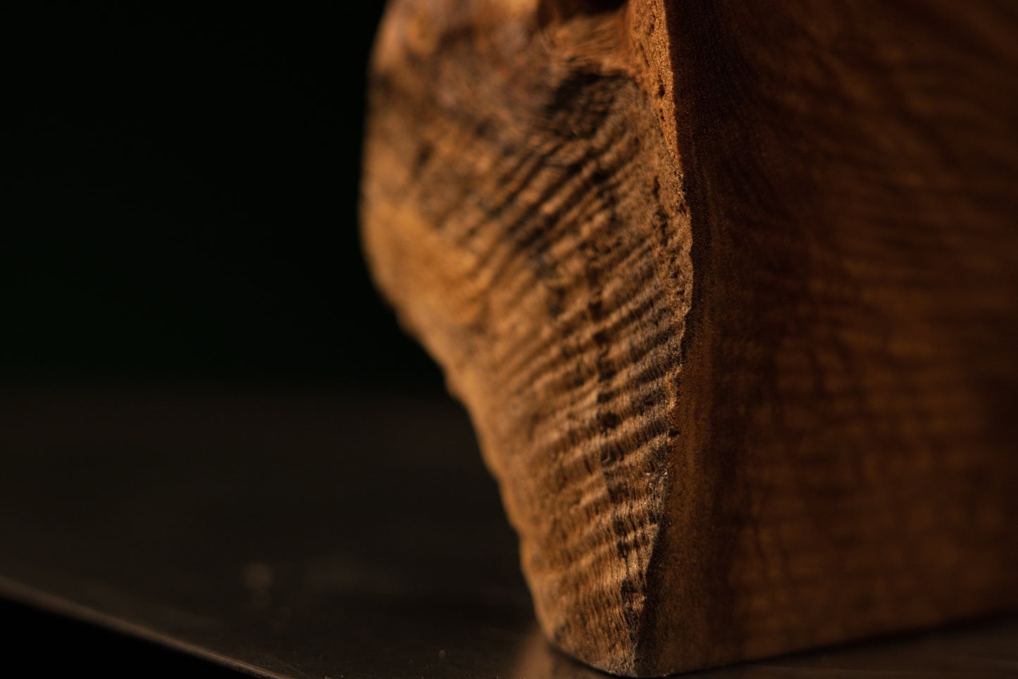Macro shot centering on a small dark circular knot surrounded by rippling golden wood grain on a luxury interior element.   