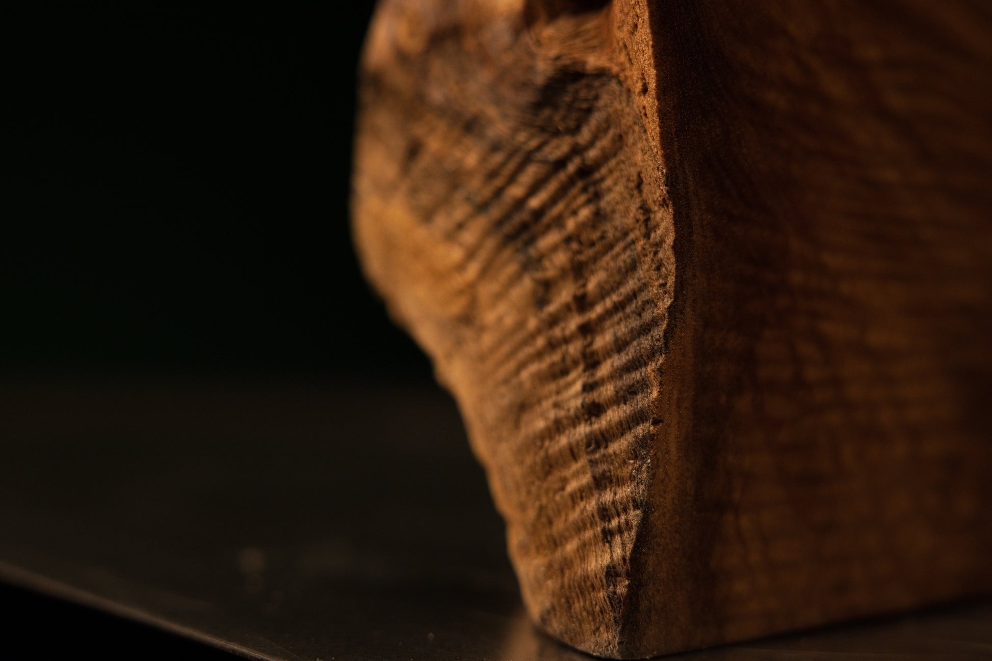 Macro shot centering on a small dark circular knot surrounded by rippling golden wood grain on a luxury interior element.   