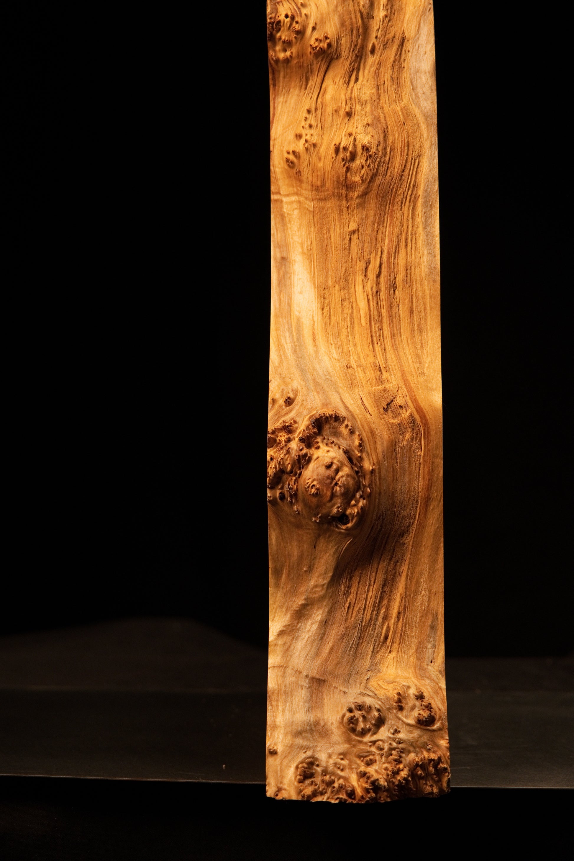 Detailed inspection of the flat precision-cut rear surface on a heritage wood piece displaying flowing grain and tiny burl eyes.   