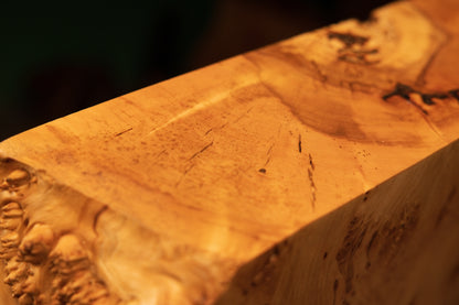 Detailed macro review of sweeping golden grain lines traversing the smooth flat upper cut of a modern resin-free biophilic wood monolith.   