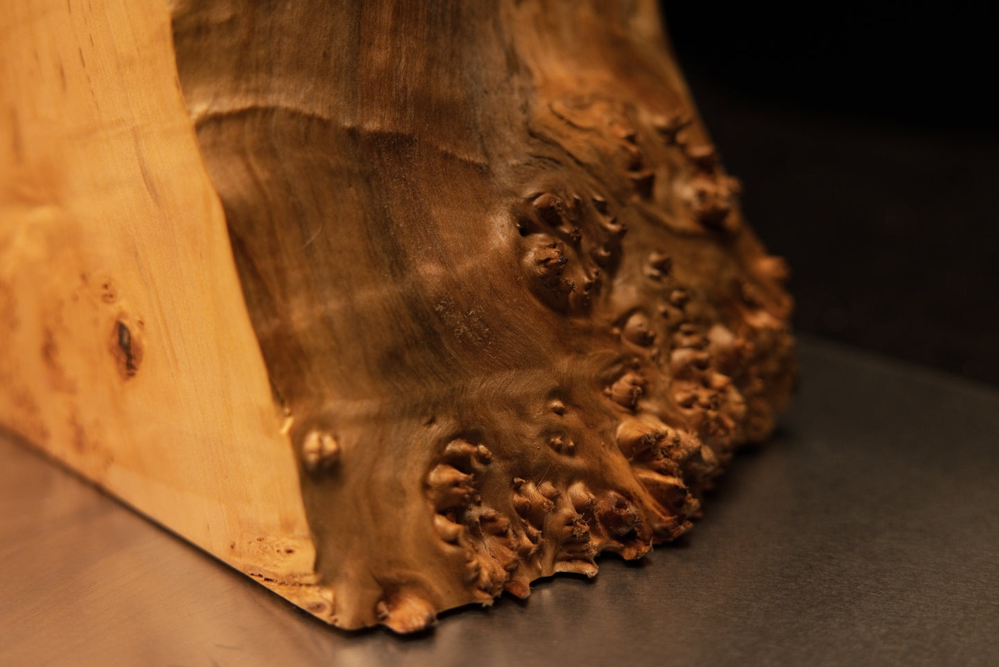 Close inspection of the lower base corner on a Relic-Grade wooden art piece showing a level bottom cut and prominent burl face.   