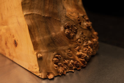 Close inspection of the lower base corner on a Relic-Grade wooden art piece showing a level bottom cut and prominent burl face.   