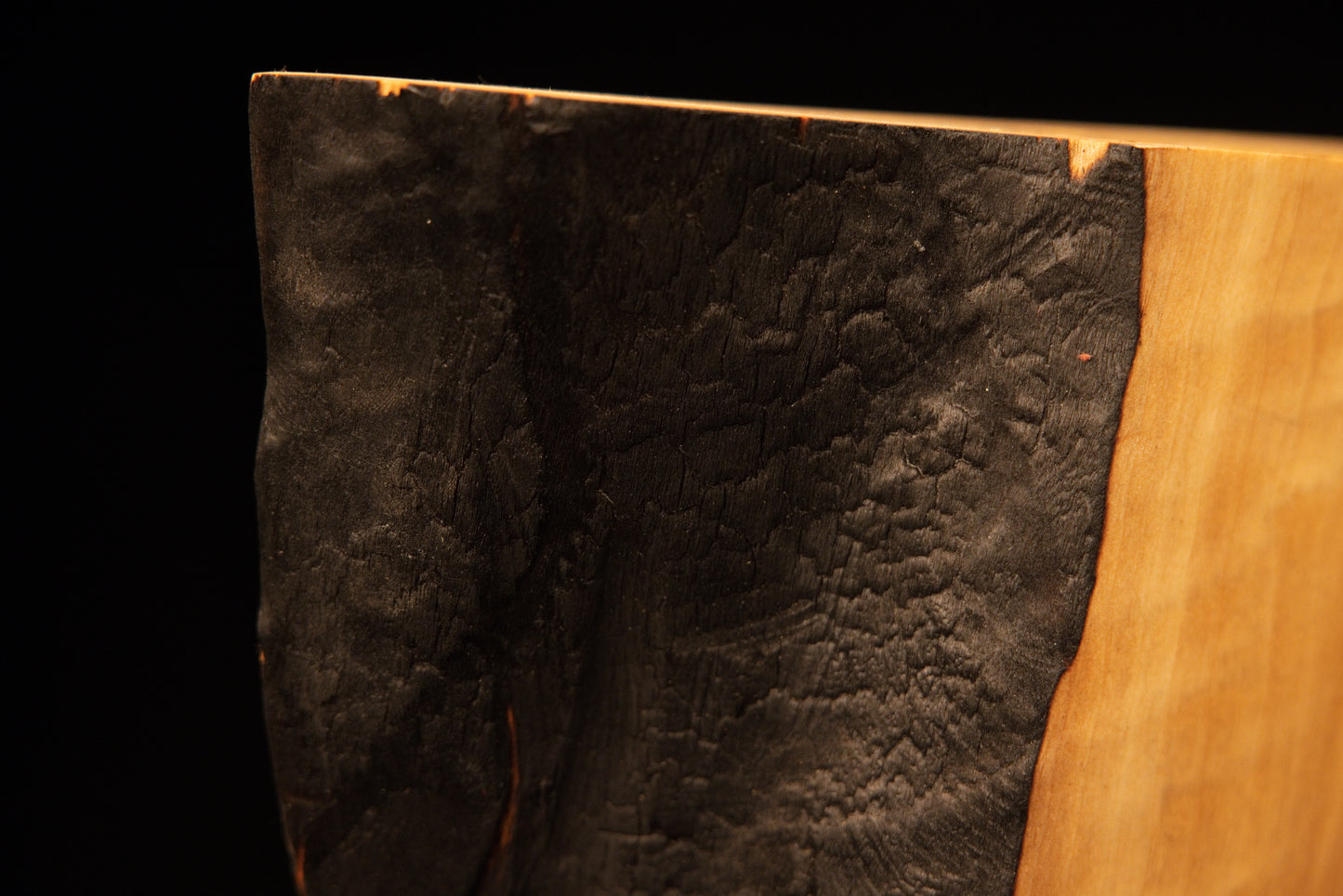 Full profile of the heavily textured dark charred side on a biophilic commercial wooden centerpiece showing genuine patina.    