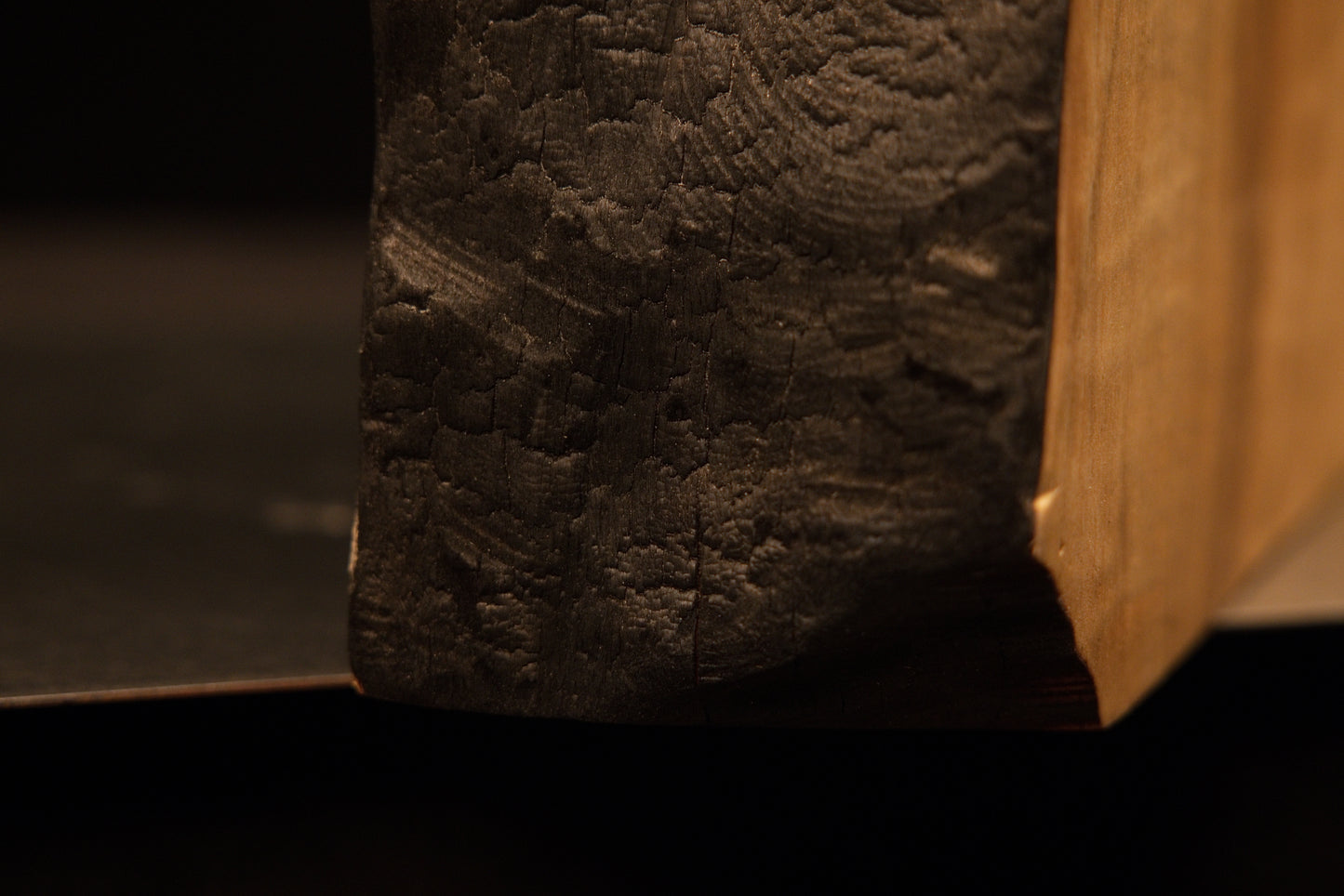 Lower corner view where the dark charred organic edge meets the flawlessly flat cut base of a climate-stable timber slab.    