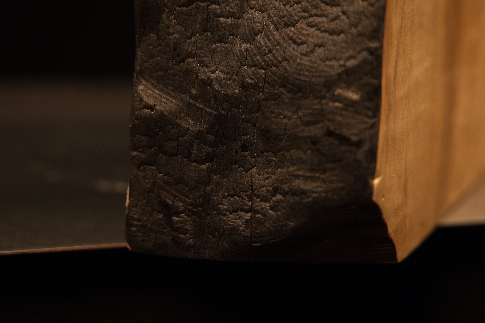Lower corner view where the dark charred organic edge meets the flawlessly flat cut base of a climate-stable timber slab.    