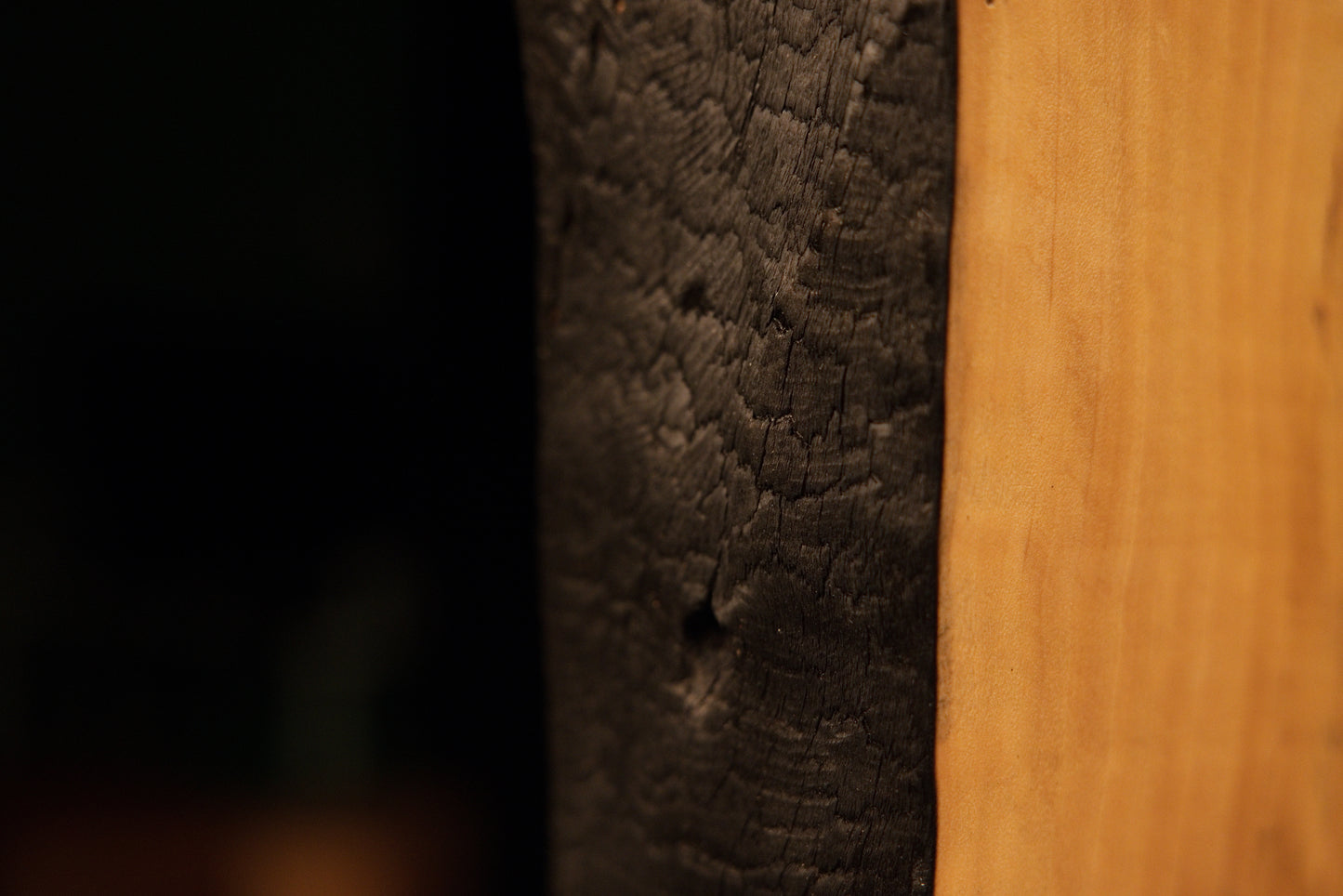 Close-up capturing the dynamic visual contrast between a deeply charred organic edge and smooth grain on a structural block.    