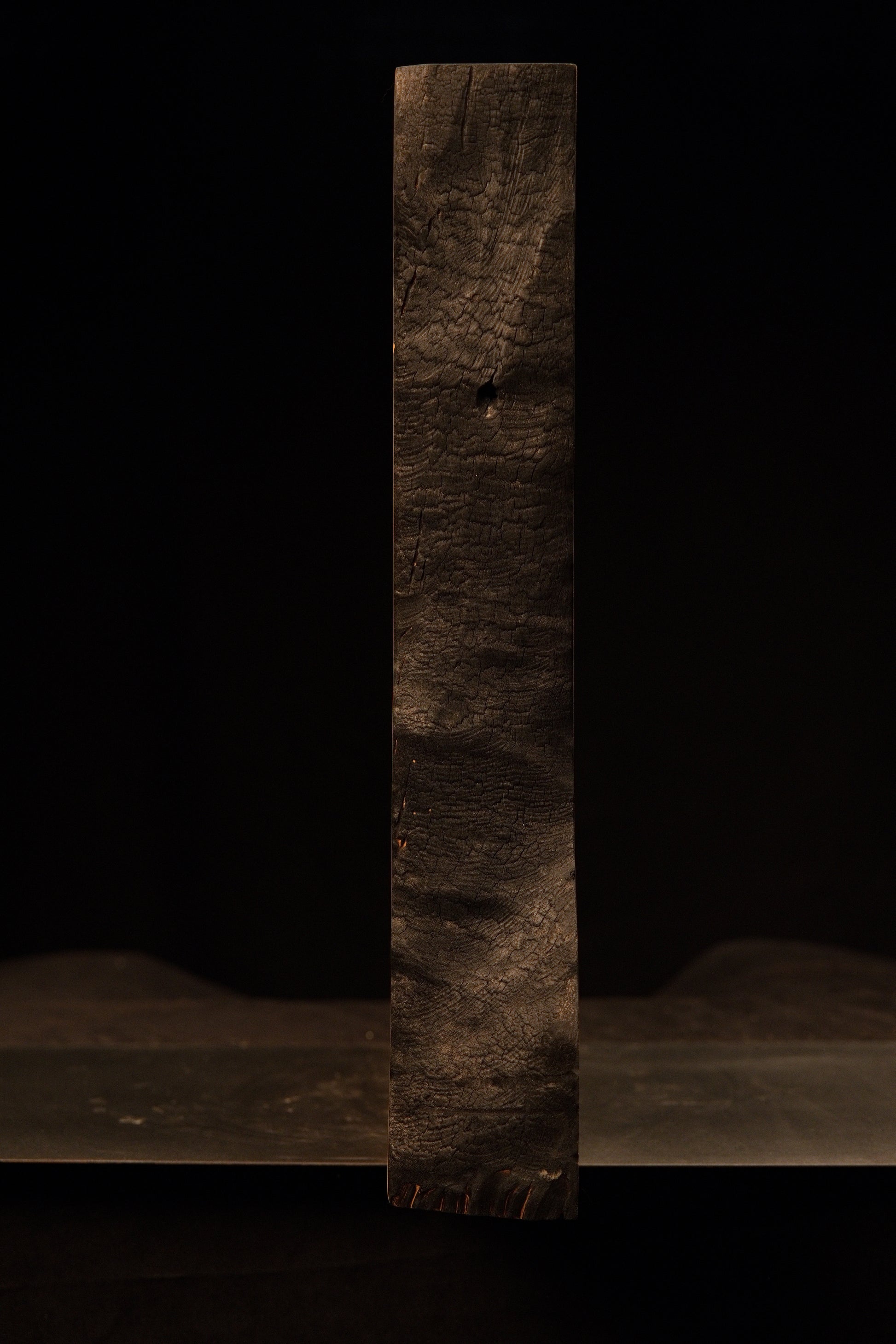 Straight vertical profile of the dark heavily textured charred face on a biophilic commercial wooden structural centerpiece.    