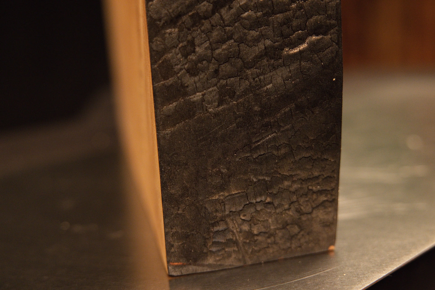 Extreme macro of a heavily textured dark side edge contrasting with a smooth horizontal top cut on a biophilic wood monolith.[cite: 3, 4]