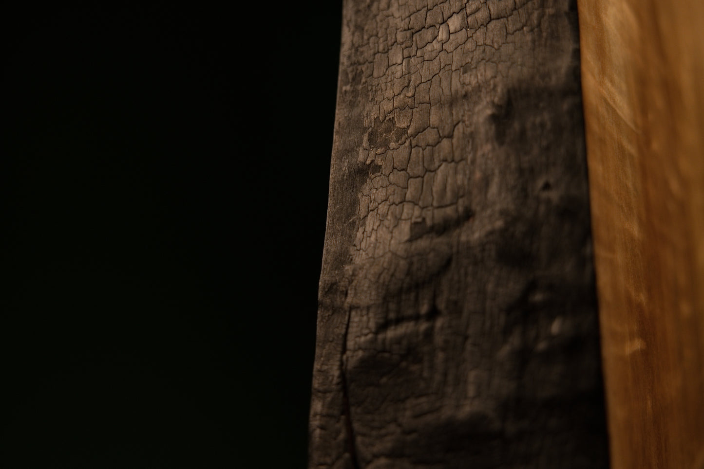 Top corner view highlighting the sharp intersection of a precision flat cut and a heavily charred side on an architectural log.  