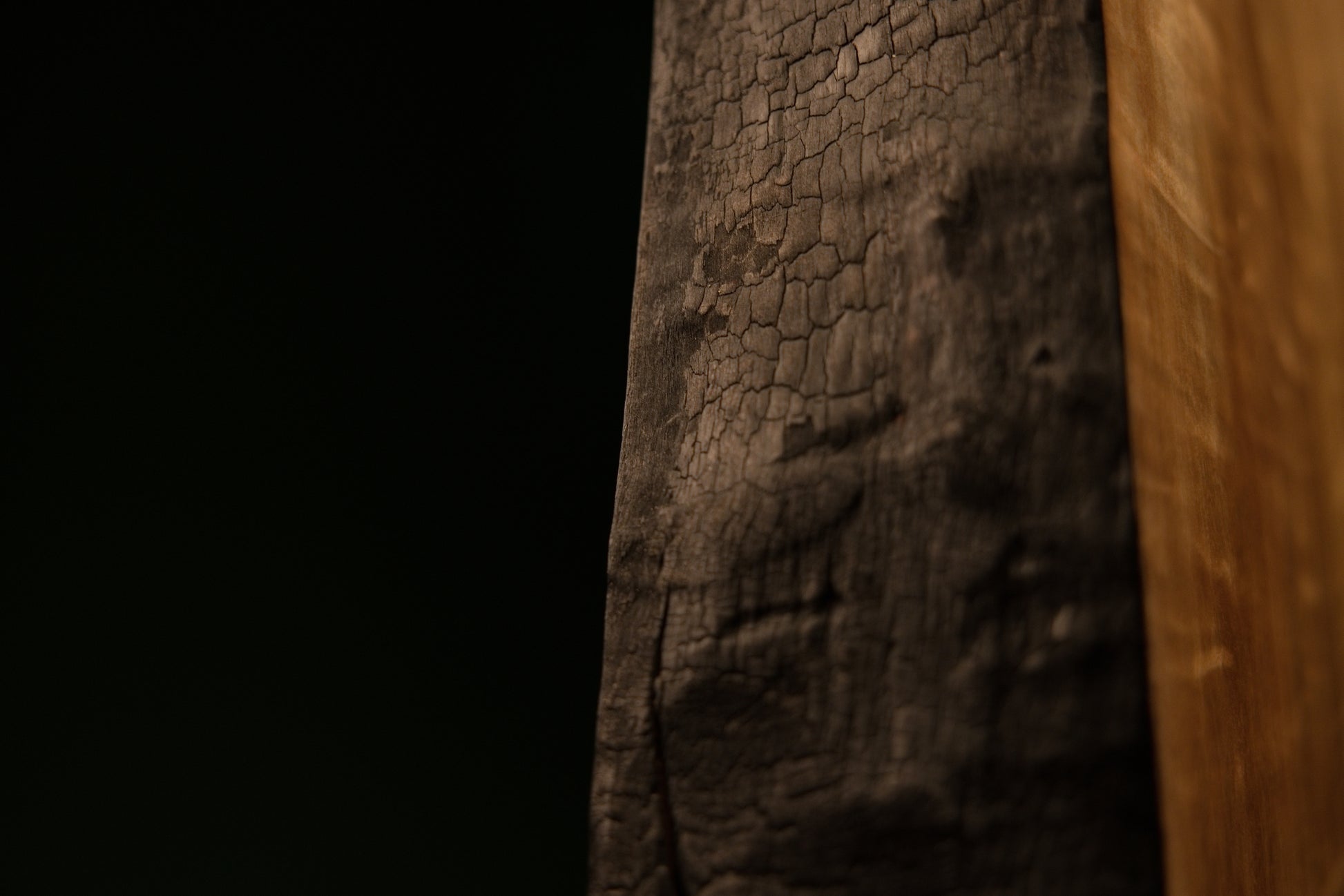 Top corner view highlighting the sharp intersection of a precision flat cut and a heavily charred side on an architectural log.  