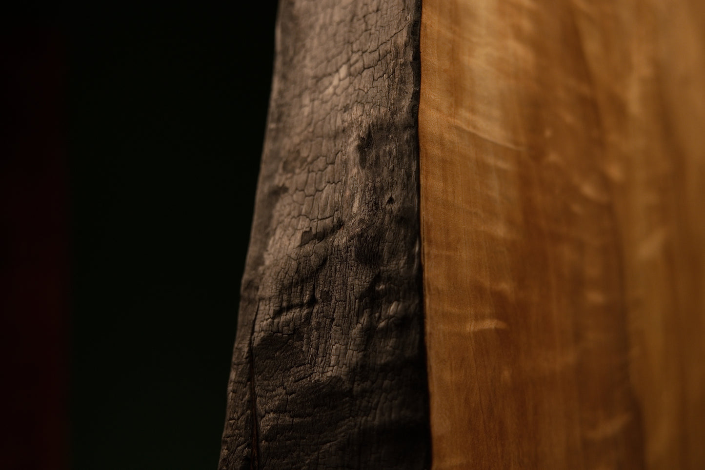 Lower corner macro where a deeply charred structural edge meets the flawlessly flat precision cut base of a timber centerpiece.  