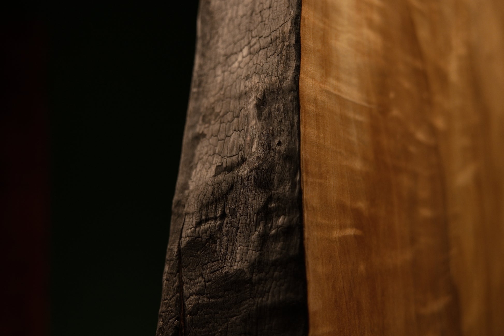 Lower corner macro where a deeply charred structural edge meets the flawlessly flat precision cut base of a timber centerpiece.  