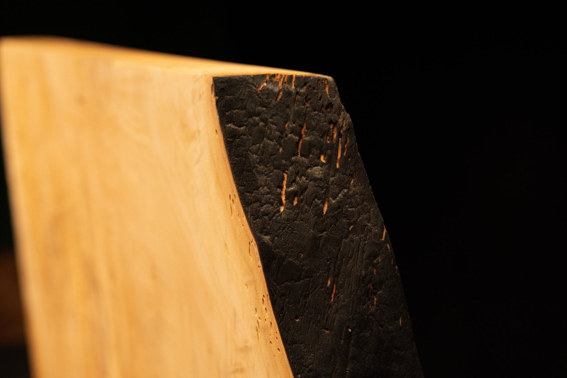 Angled profile of a solid epoxy-free biophilic timber element showcasing smooth vertical grain meeting a dark charred side edge. 