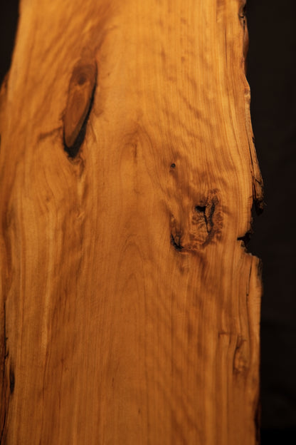 Close-up of smooth flowing grain suddenly interrupted by a dark organic knot and deep vertical fissures on a structural log. 