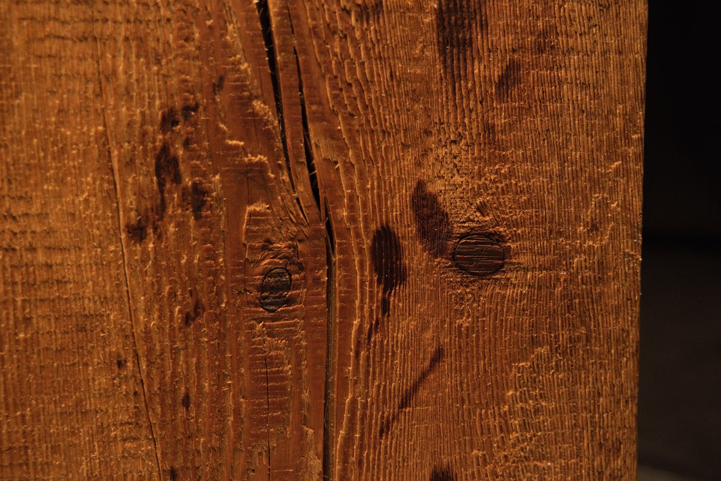 Close detail of small dark organic knots and scattered biological marks within the sweeping grain of a structural timber element. 