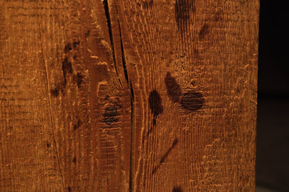Close detail of small dark organic knots and scattered biological marks within the sweeping grain of a structural timber element. 
