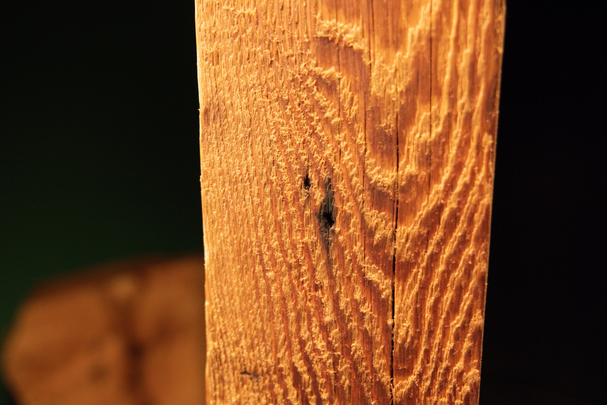 Close detail of an authentic dark knot and deep vertical channeling along the sharp corner of a biophilic architectural centerpiece. 