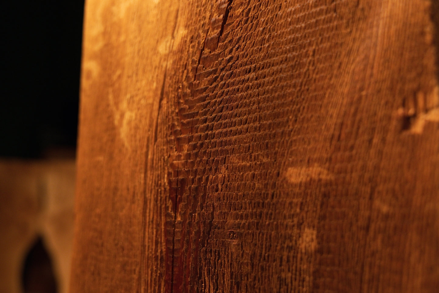 Close view of a dark biological knot positioned near a stabilized vertical fissure on a highly textured architectural wood surface. 