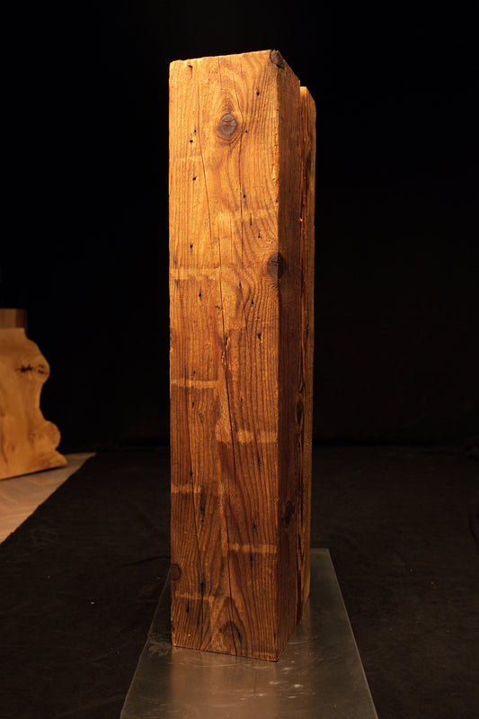 Full standing view of a tall climate-stable structural timber beam displaying tight vertical grain and multiple dark knots. 