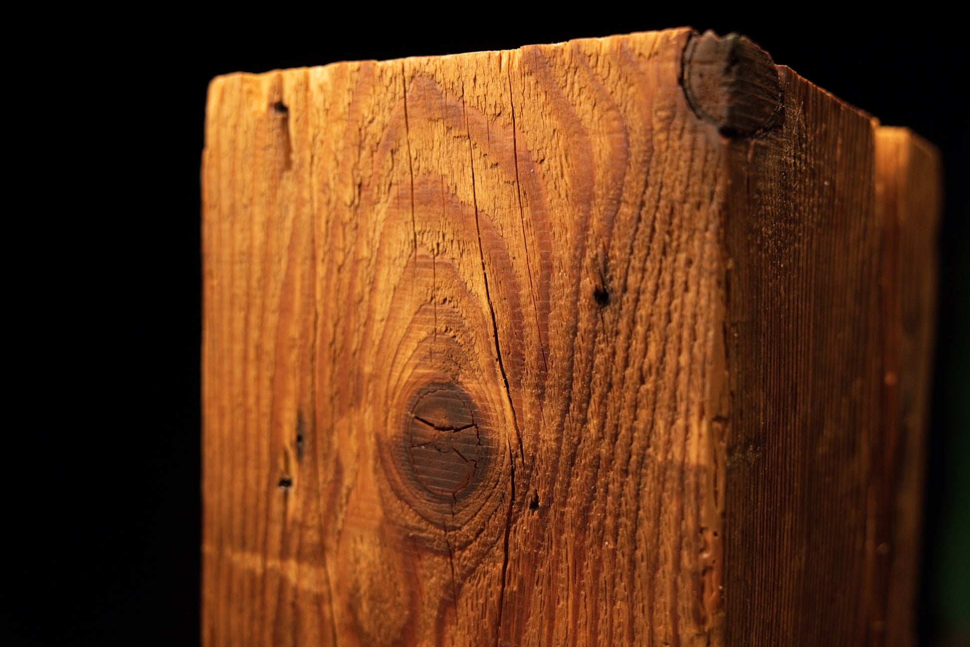 Close detail of a dark biological knot intersecting the sharp vertical corner edge of an epoxy-free structural wooden slab. 