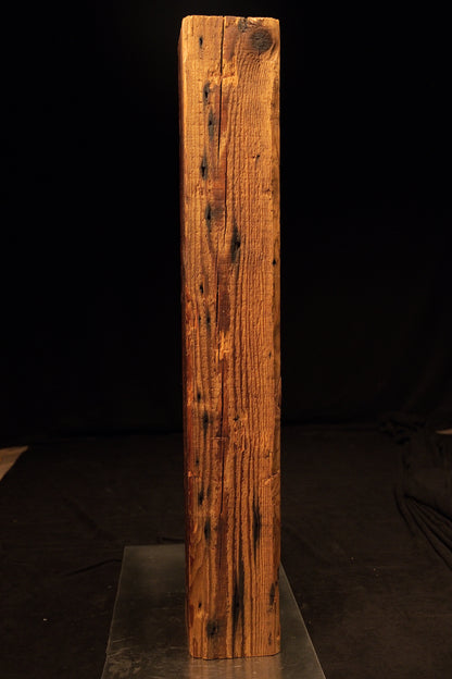 Full vertical view of a tall climate-stable structural timber beam displaying tight vertical grain and multiple dark nail voids.  