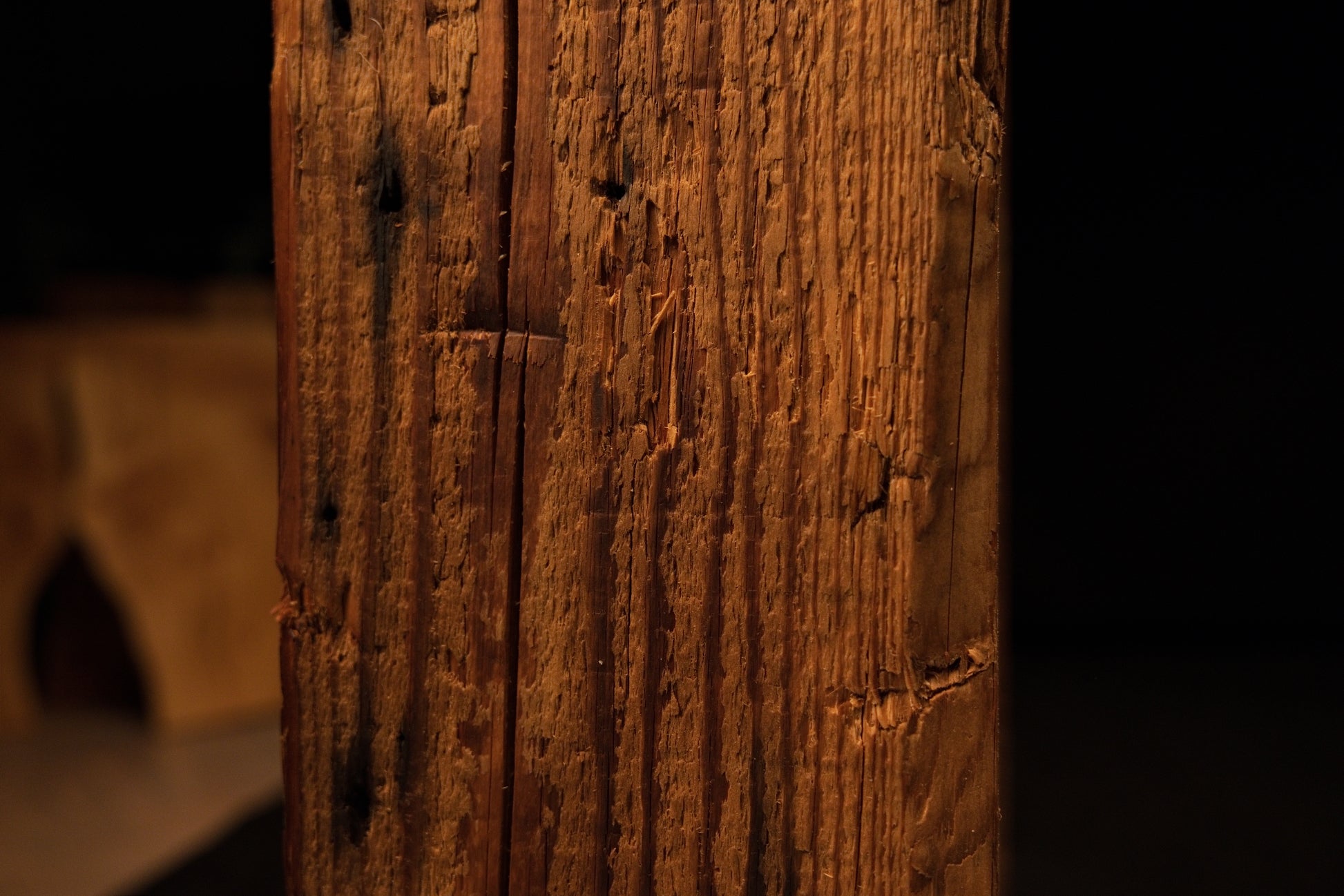 Close detail of a dark biological knot intersecting the sharp vertical corner edge of an epoxy-free structural wooden slab.  